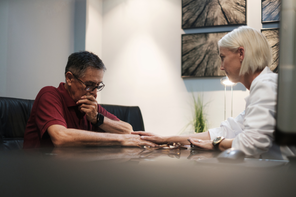 A concerned man speaks with a professional woman in an office setting, possibly discussing the emotional impact of a medical misdiagnosis.  