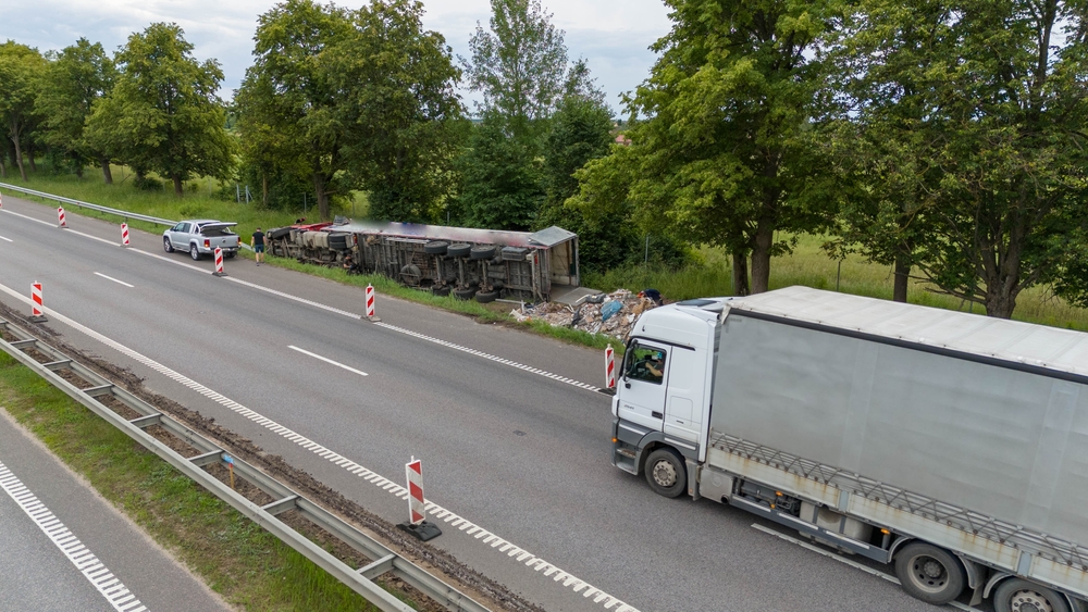 Overturned trailer and scattered debris from a truck accident on a divided highway with traffic diverted and emergency response on site.