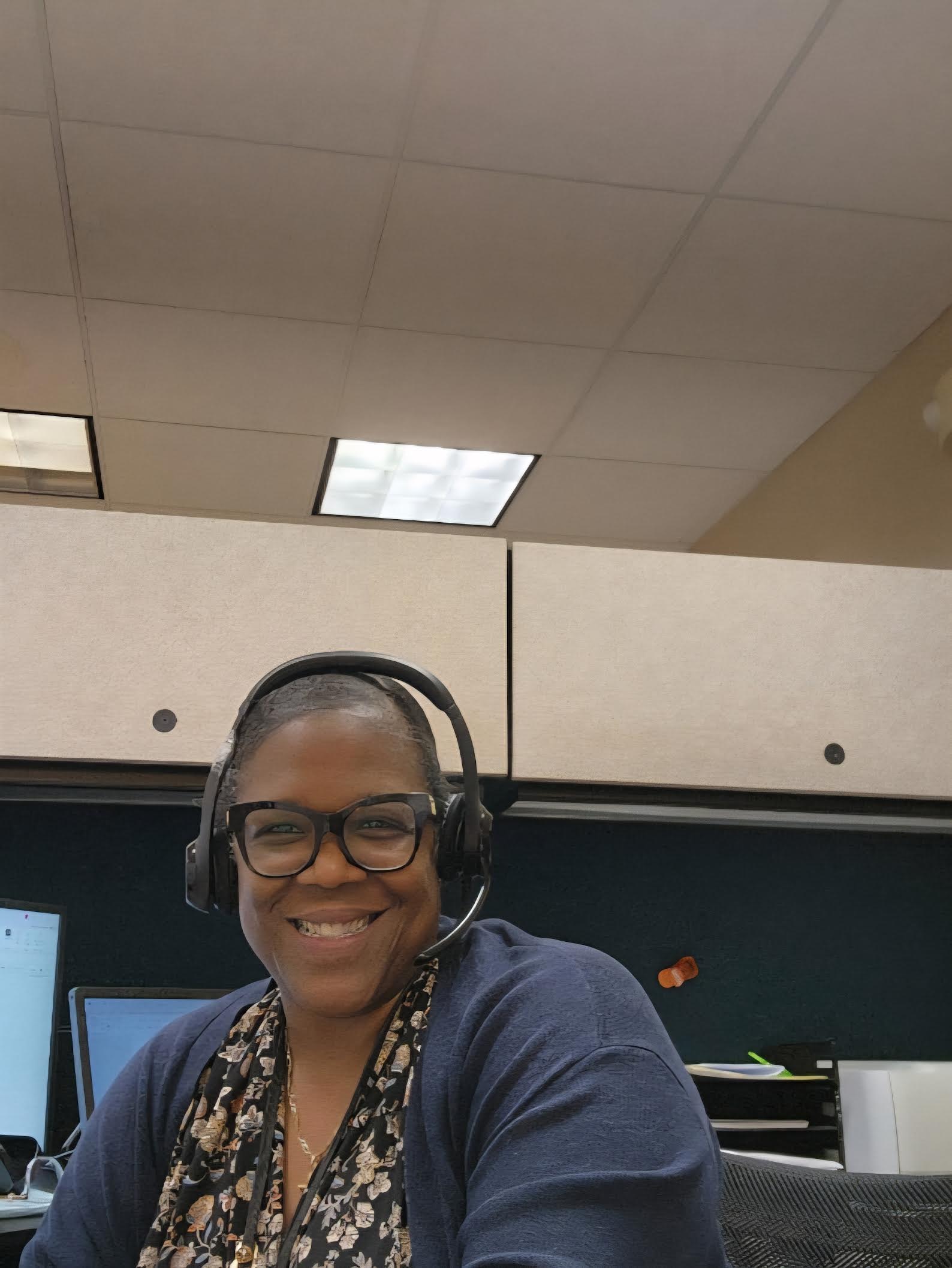 Smiling in-house legal nurse consultant at Blume Forte Attorneys at Law wearing a headset and glasses, seated at her office cubicle with computer monitors in the background.  