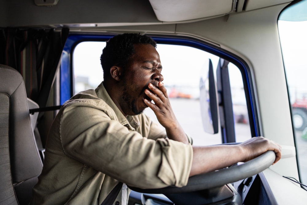 Tired truck driver yawning behind the wheel, highlighting the risks of drowsy or overworked driving and whether you can sue after a crash.  