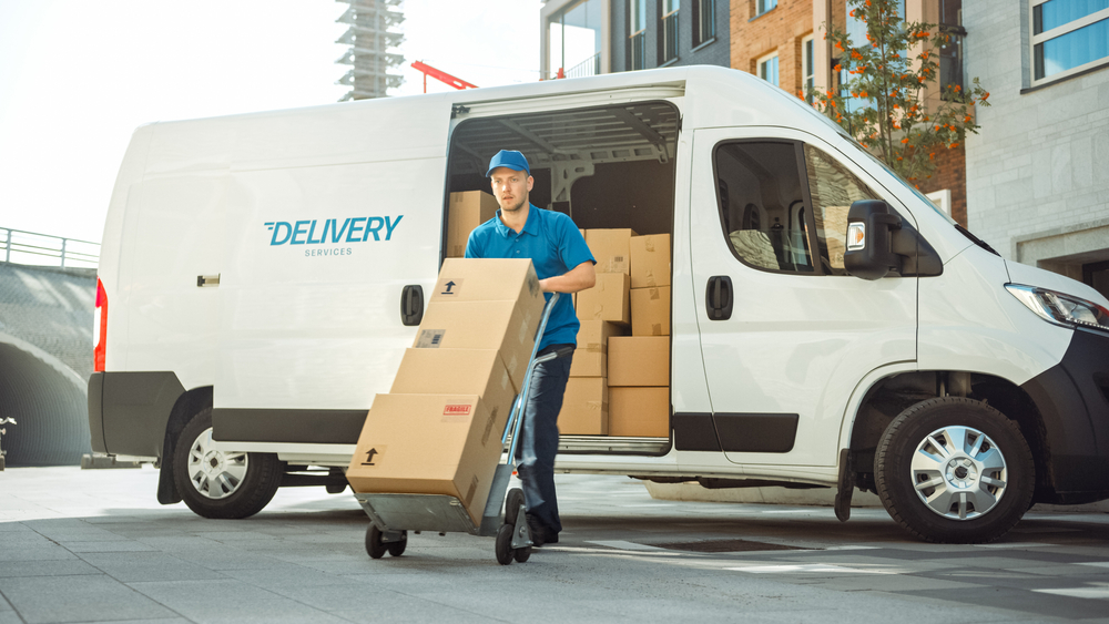 A delivery driver unloads packages from a white delivery truck parked in a residential neighborhood, where accidents involving pedestrians or residents can lead to injury claims.