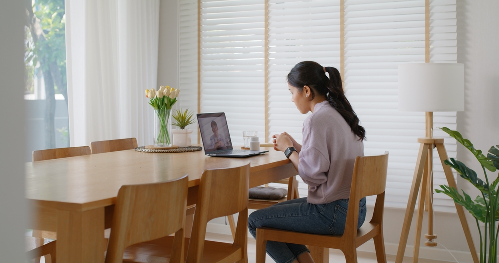 Woman sitting at a dining table on a telehealth video call, raising the question: Are You a Victim of Medical Malpractice If Your Telehealth Doctor Missed a Major Symptom?