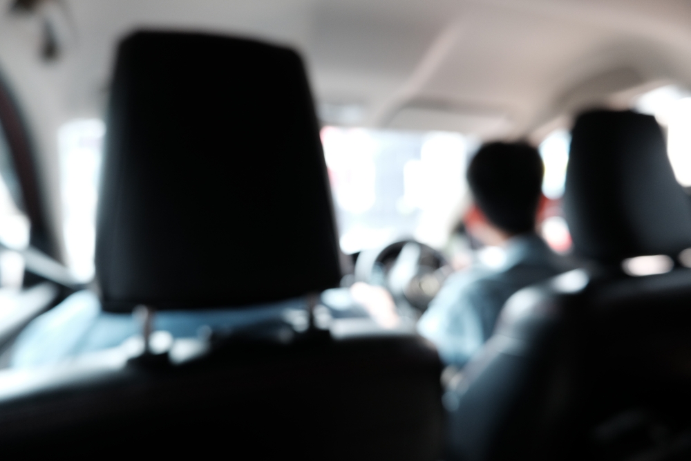 Blurry view from the backseat of a rideshare car, showing a driver at the wheel, symbolizing potential safety risks for Uber passengers.