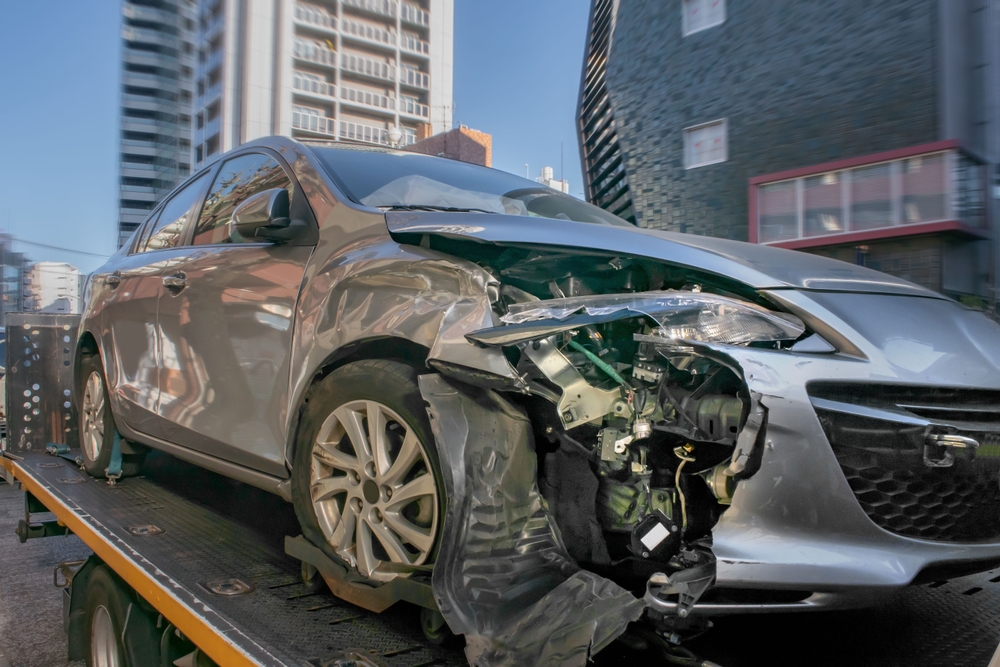 Damaged silver car on a tow truck after being injured by a truck accident.