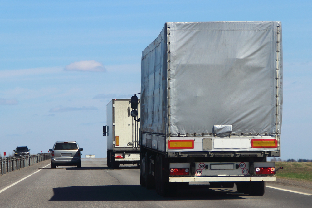 A car drives alongside two large trucks on the highway, illustrating how overloaded trucks increase accident liability.