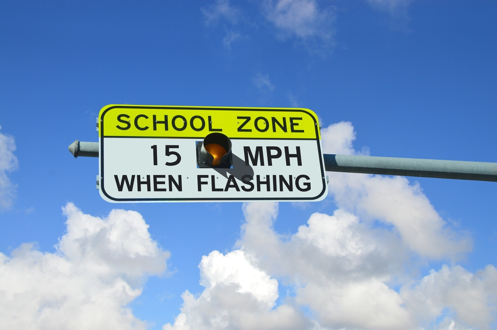 School zone speed limit sign showing 15 MPH when flashing under a bright blue sky, representing safety rules and awareness to prevent school zone car accidents.