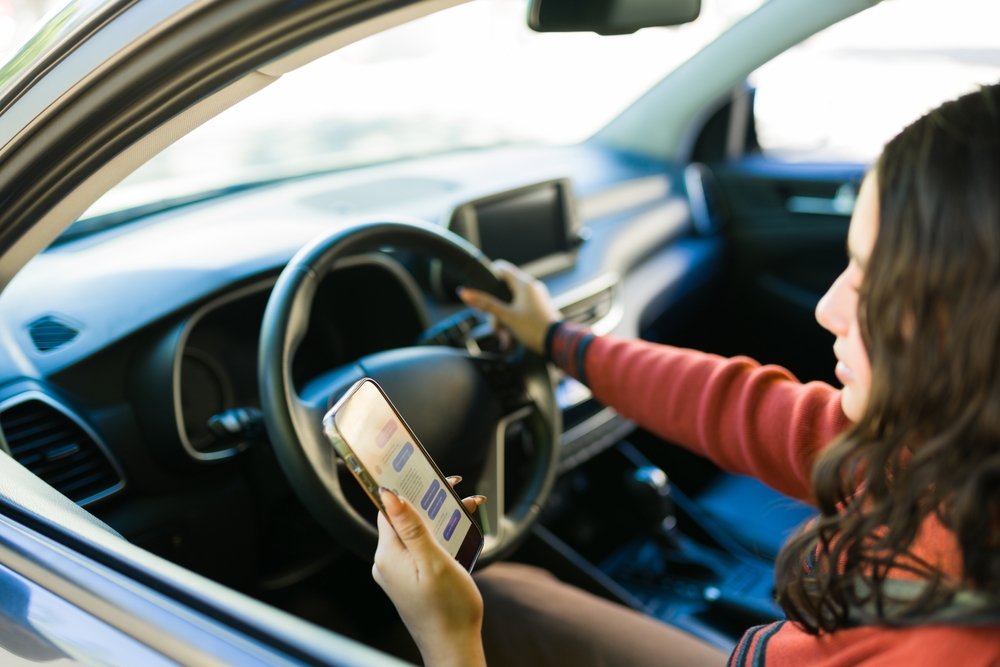 Teen driver looking at a phone while sitting behind the wheel, illustrating distracted driving risks.