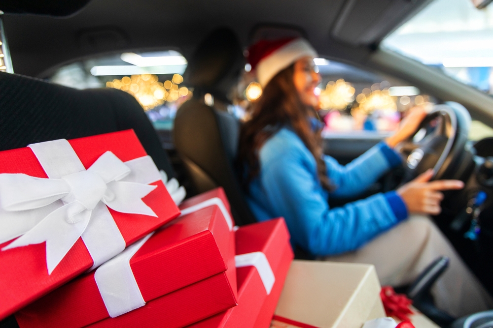 A woman wearing a Santa hat drives a car filled with wrapped Christmas gifts, illustrating Christmas travel safety and holiday driving in New Jersey.