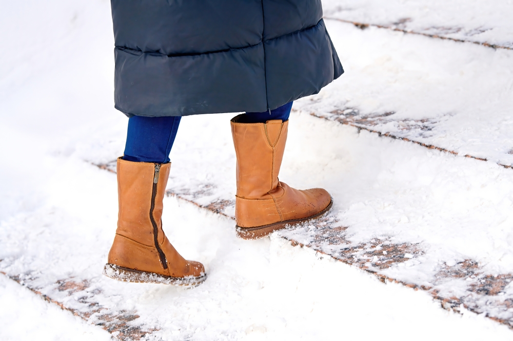 A pedestrian wearing winter boots carefully navigating snow-covered outdoor stairs, a common site for a slip and fall accident in New Jersey.