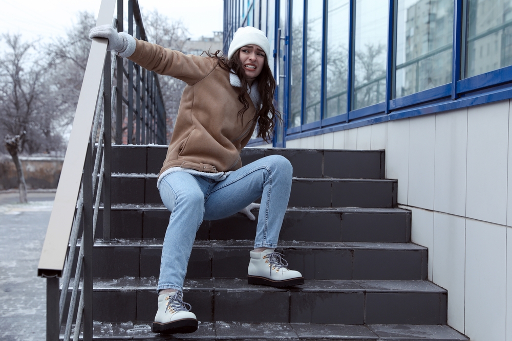 A woman sitting on icy steps holding a handrail after a slip and fall accident, emphasizing the need for immediate medical care and documentation.