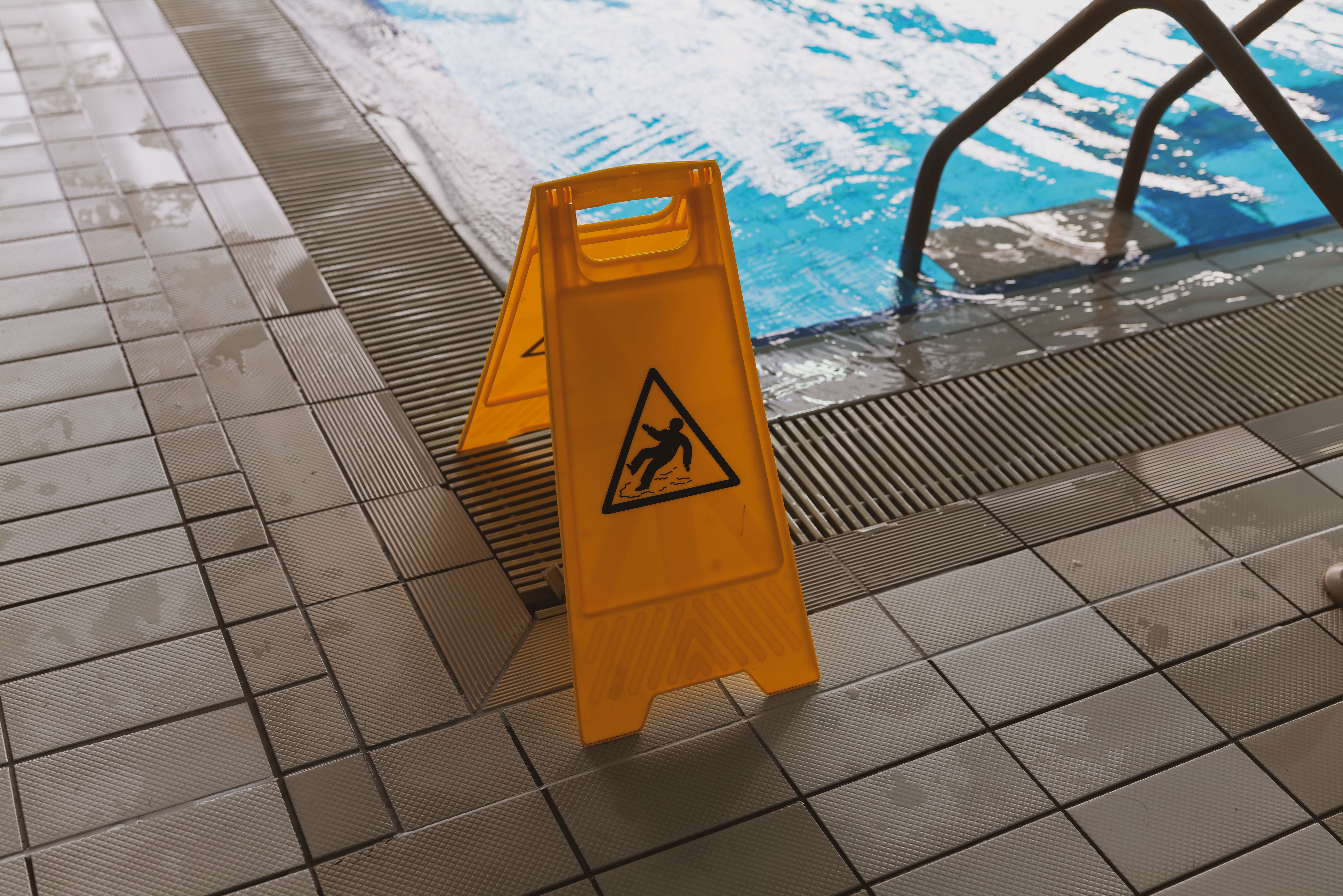 Wet floor caution sign beside a pool, illustrative image representing the rise in summer slip and fall injuries across New Jersey.