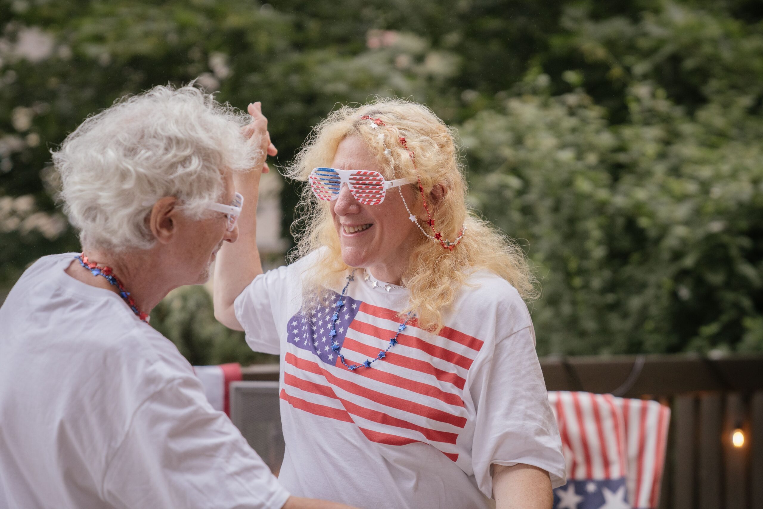 Two smiling guests wearing American flag shirts and patriotic accessories at a backyard Fourth of July party.