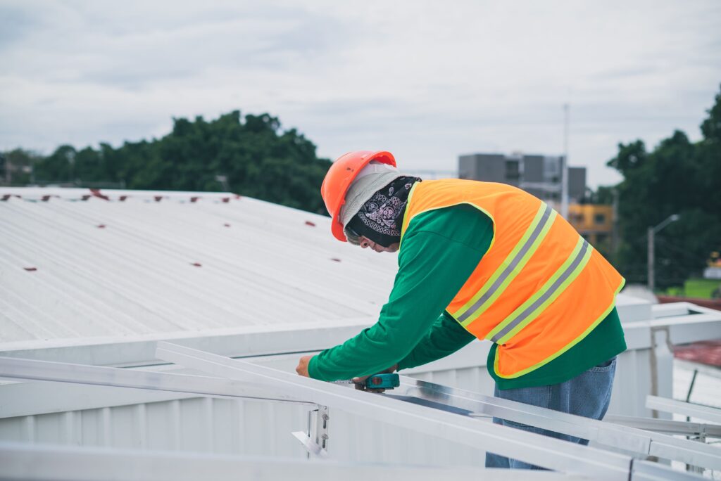 Roofer in a hard hat and safety vest working on a metal roof under the hot sun, illustrating heat illness risk on New Jersey roofing crews.