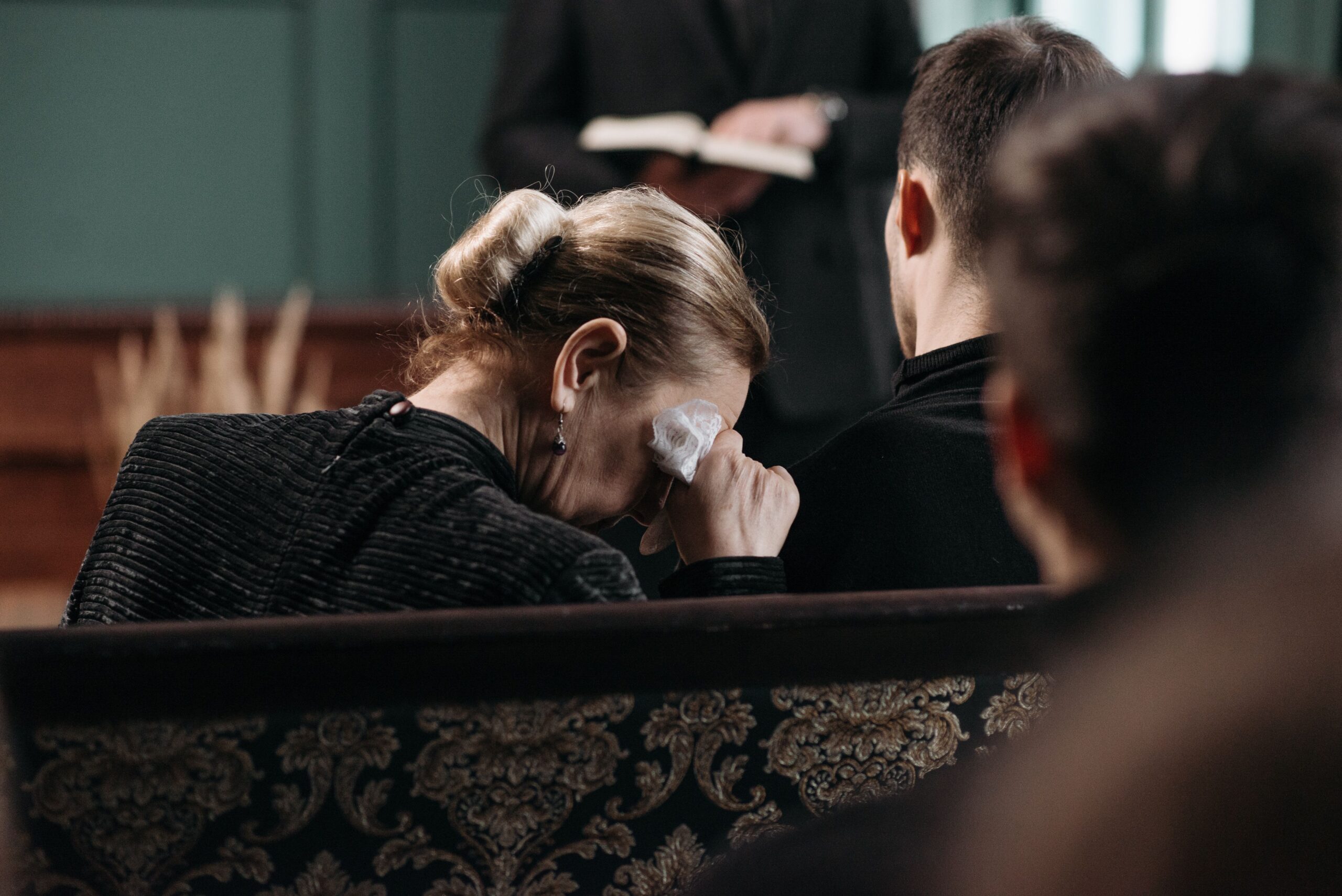 Grieving woman wiping tears at a funeral while a man comforts her, reflecting a New Jersey wrongful death loss.