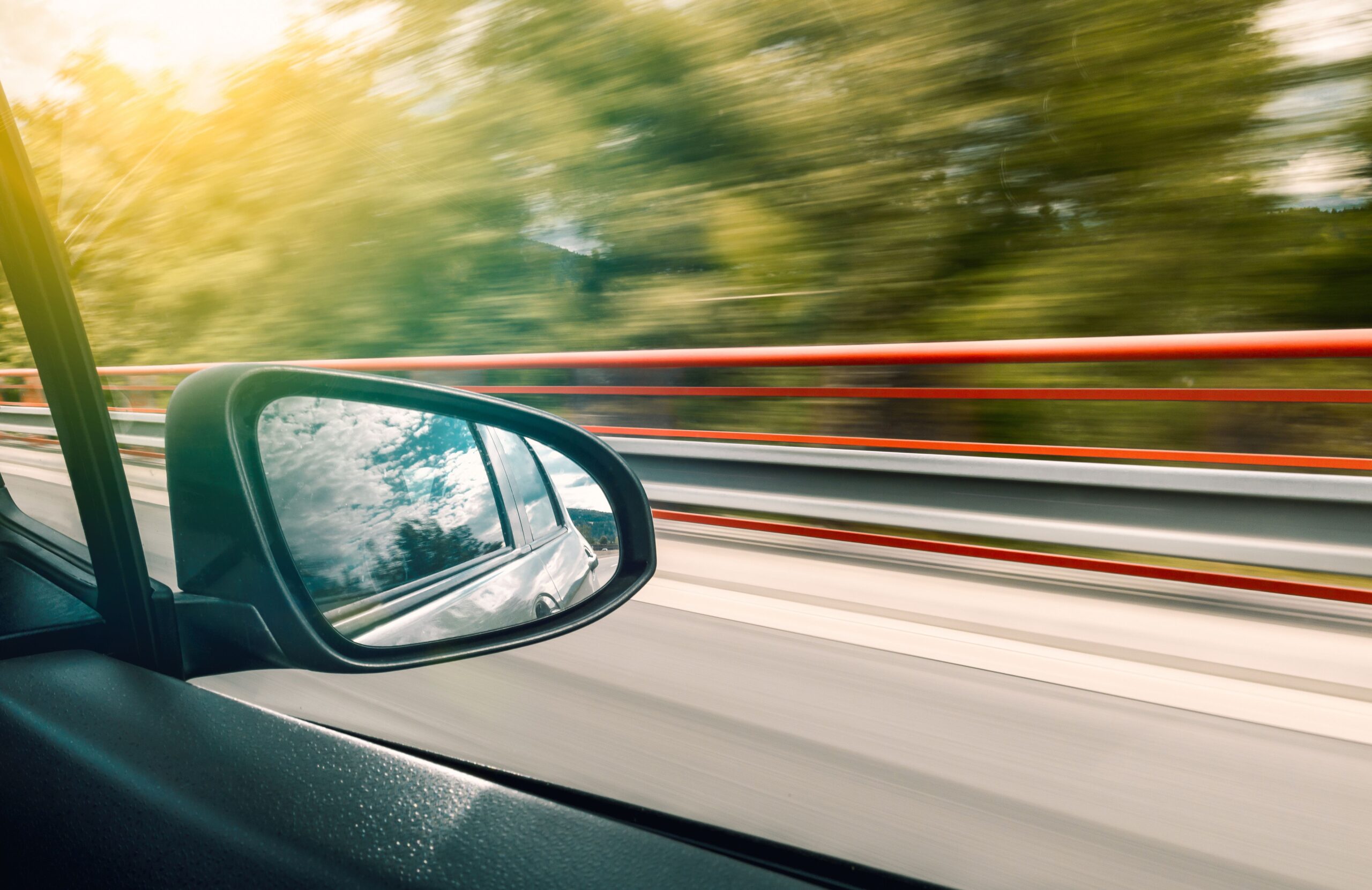 View of a highway and guardrail seen through a car side mirror while driving, illustrating car accident risks during Labor Day weekend in New Jersey.
